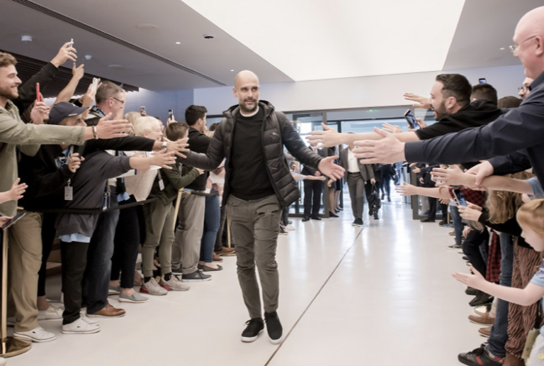 Manchester City Manager Pep Guardiola walking through the Tunnel Club area at the Etihad Stadium, high-fiving excited fans.